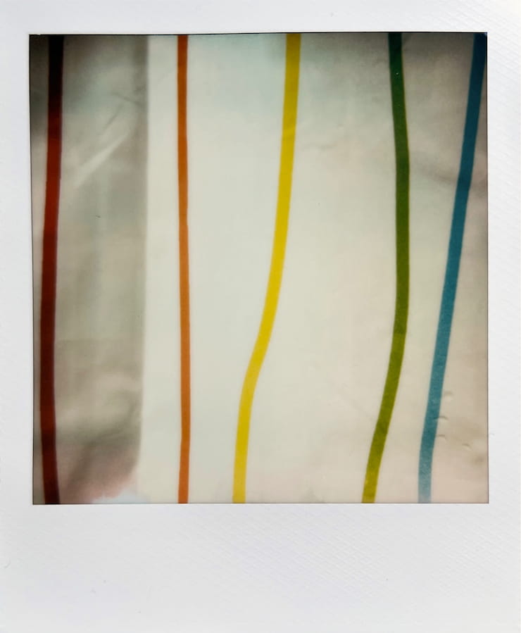 A white fabric with colourful thin vertical lines. From the
      left, one in red, one in orange, then yellow, green and blue. You can spot
      the occasional water drop.