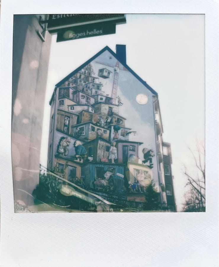 The side of a multi-story house, colourfully painted with small
      houses in comic style.