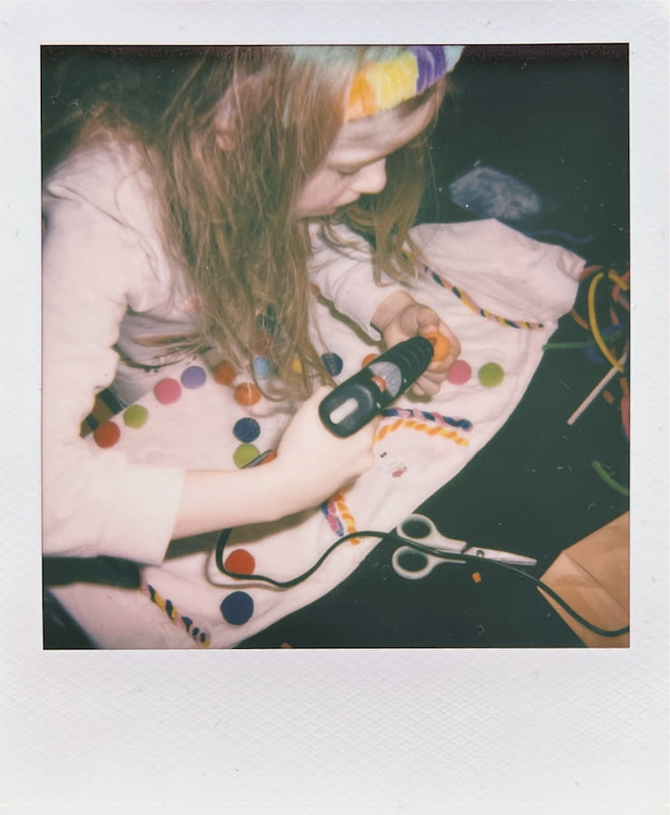 A child with a table full of hot-glueing colourful ball onto a
      t-shirt.