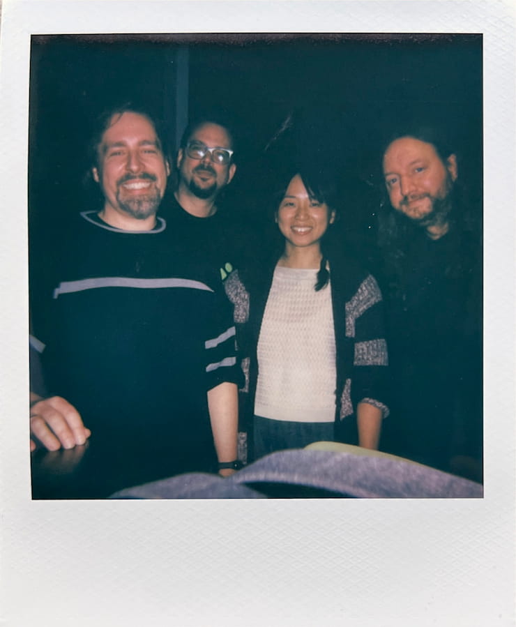 Three men and one woman looking into the camera smiling in front
      of a black background.