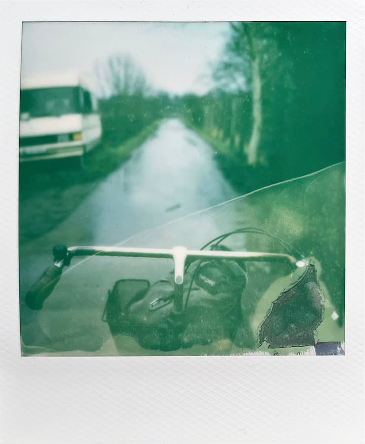 Handlebars of a holland bike. In the background a path with
      vegetation on both sides and a motorhome on the left.