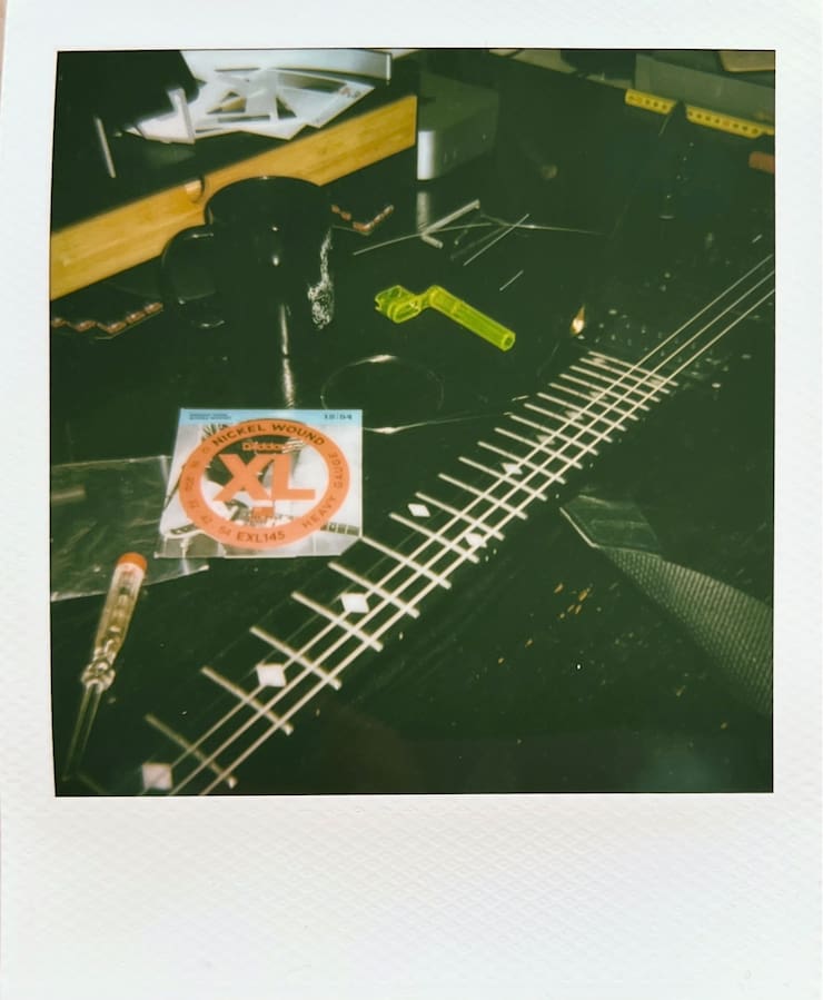 My black V-shaped guitar on my black desk. Guitar string
      packaging and tools around it.
