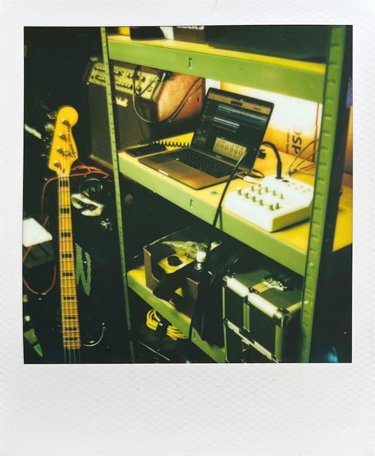 A cupboard with a laptop and an audio interface in a rehearsal
      space. A bass guitar and amps next to it.