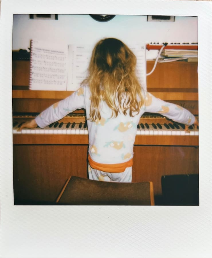A girl playing a wooden piano photographed from behing.