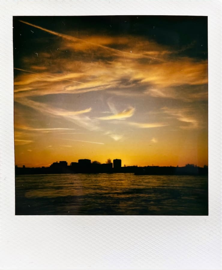 A sunset with clear skies, building silhouettes in the back and
      a river down at the front.