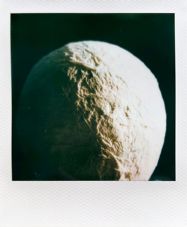 A white sphere-like shape with texture, lit on the right half,
      looking similar to the moon.