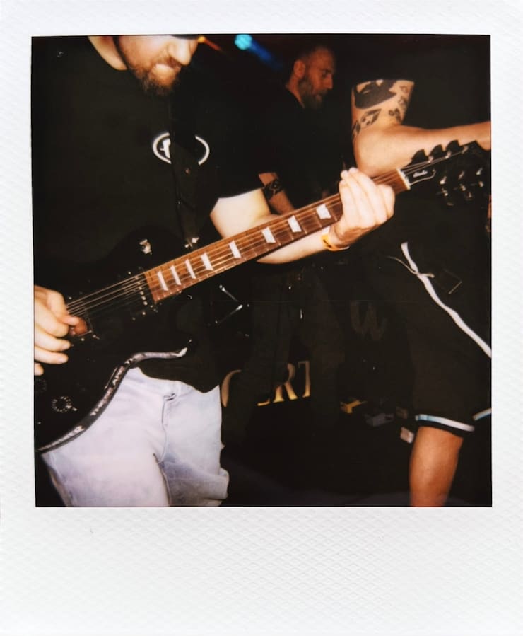Photo of a torso of a guitarist on stage. Next to him and in the
      background, further musicians are partly seen.