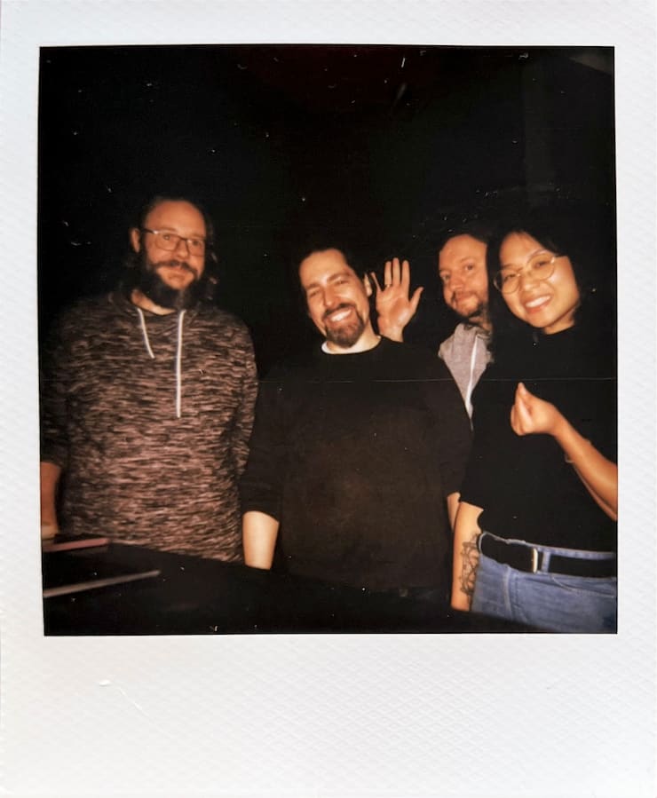 3 men and 1 woman standing in front of a black background,
      looking into the camera.