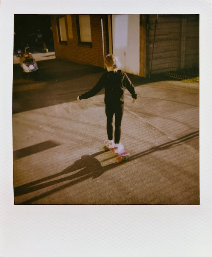 A girl on a little pink skateboard from behing. In the
      sun.
