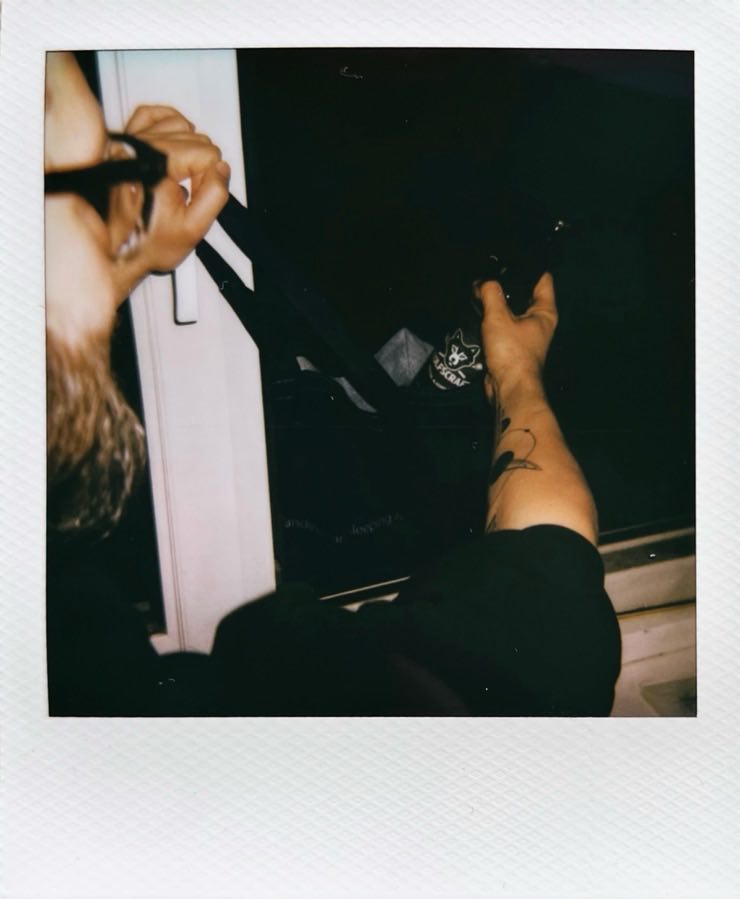 A person getting a beer from a bag hung outside a window.