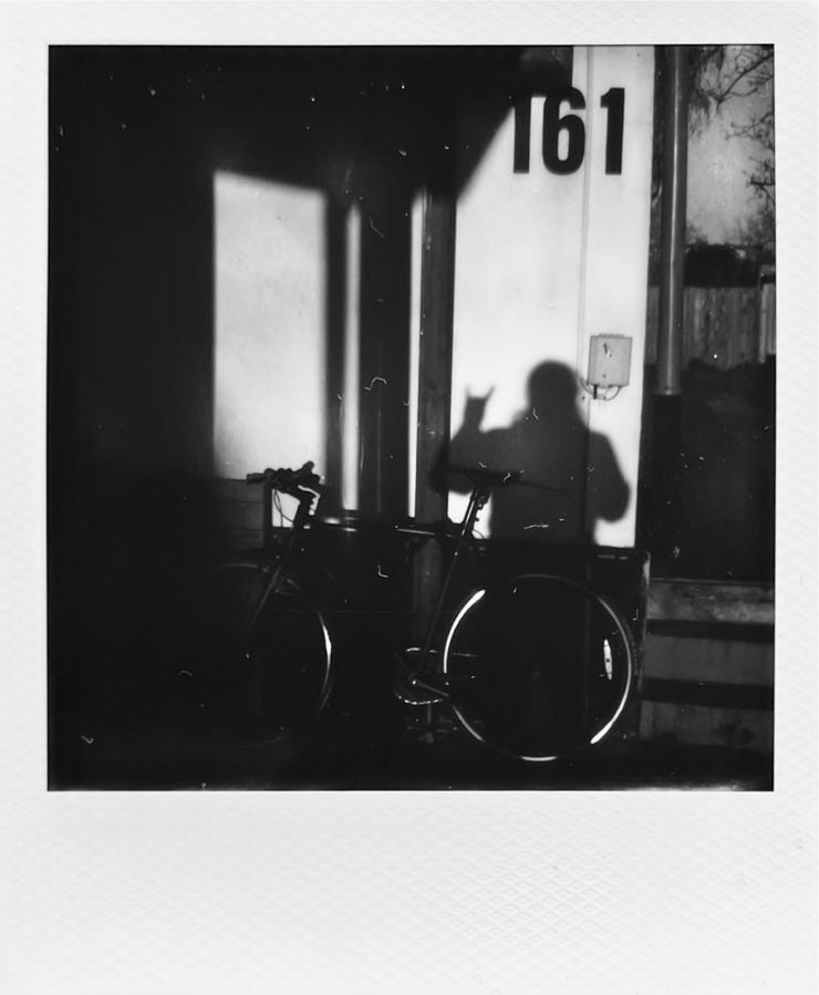 A high contrast b&w image of my bike leaning against parts of a building with the number 161.