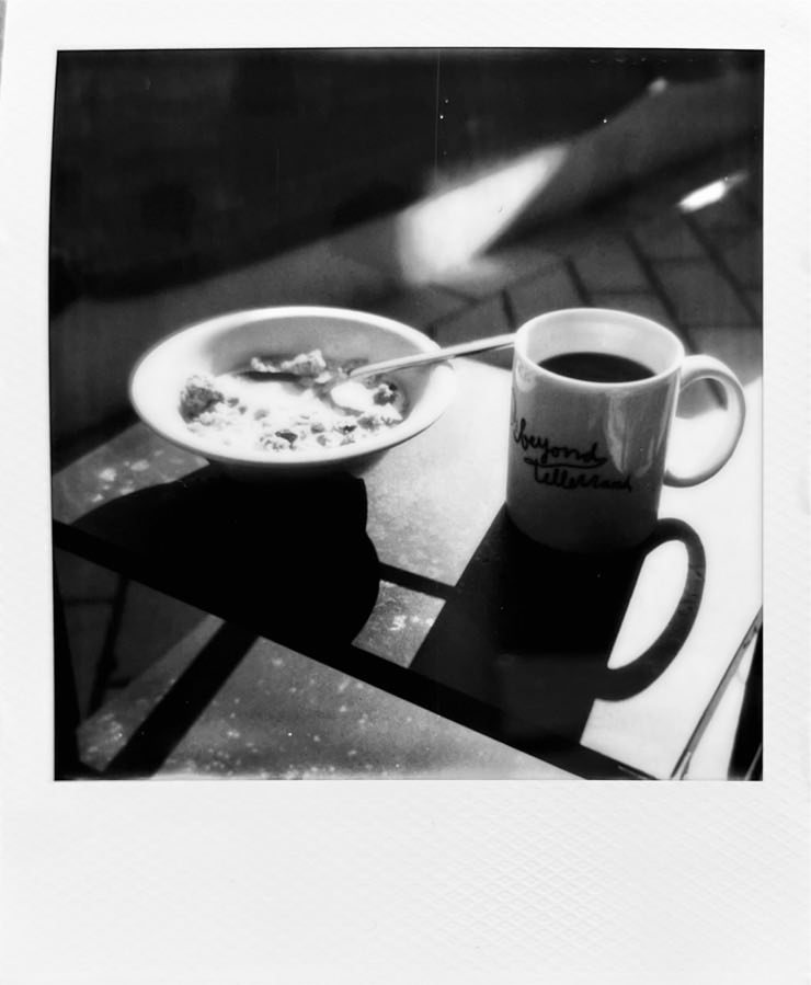A bowl of muesli and a mug of coffee on a sunlit side table.