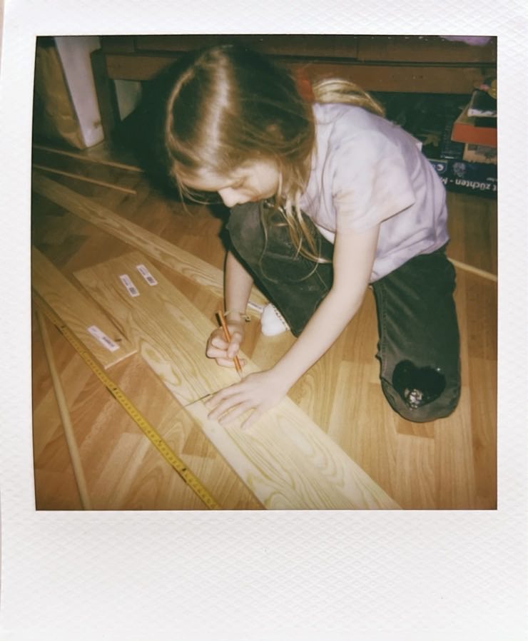 A child kneeling on the floor making pencil marks on wood.