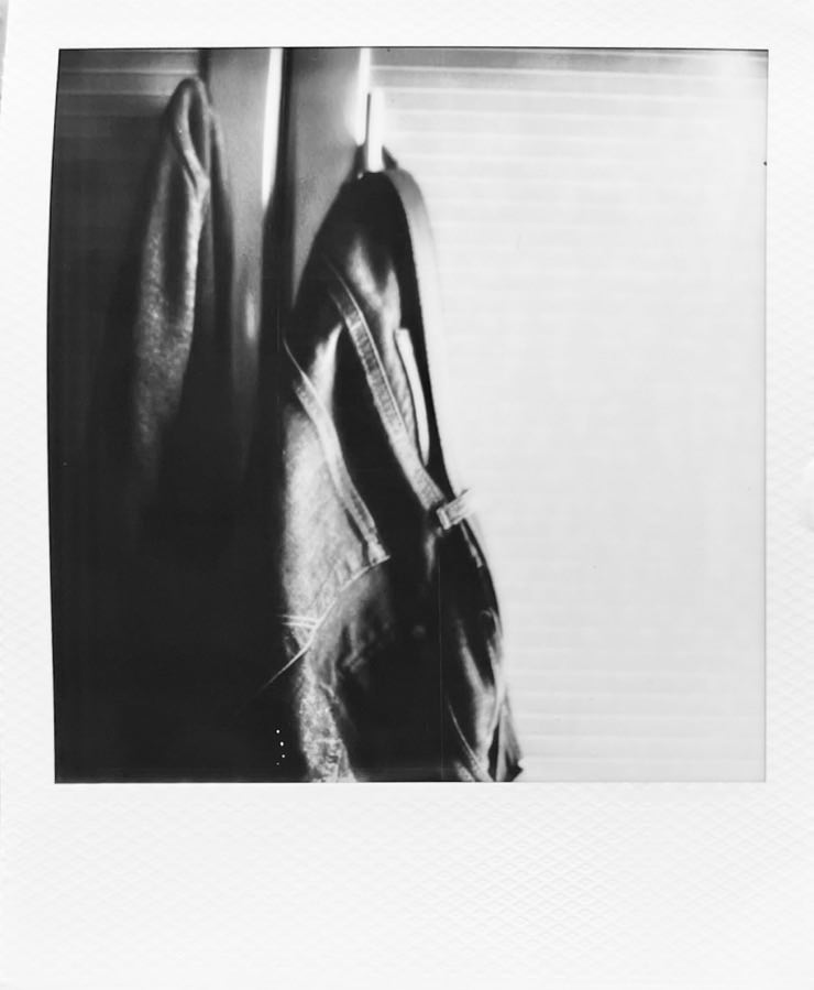 A jeans and a jacket hanging from a wardrobe next to the bed.