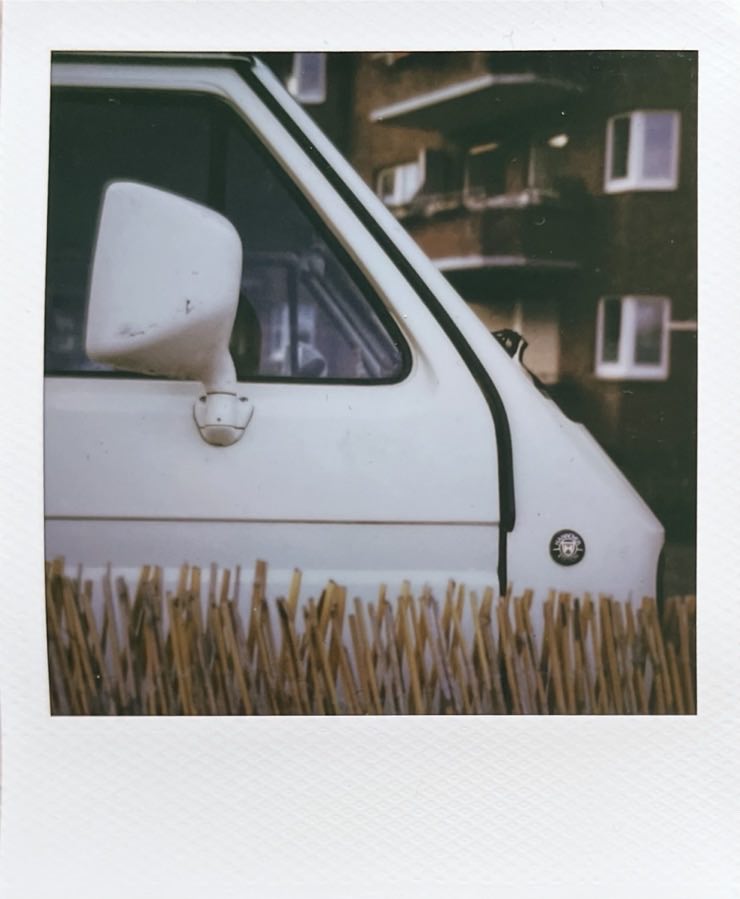 The front of a white van, photographed from the right side. The top of a bamboo fence in front.