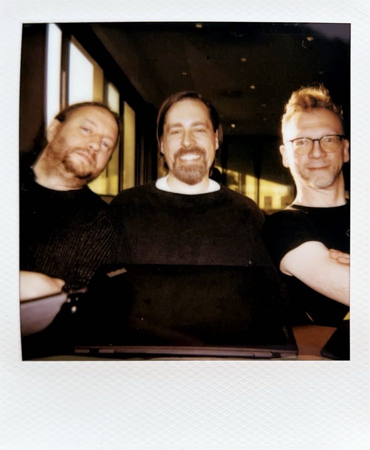 Three men sitting behind a table looking into the camera.