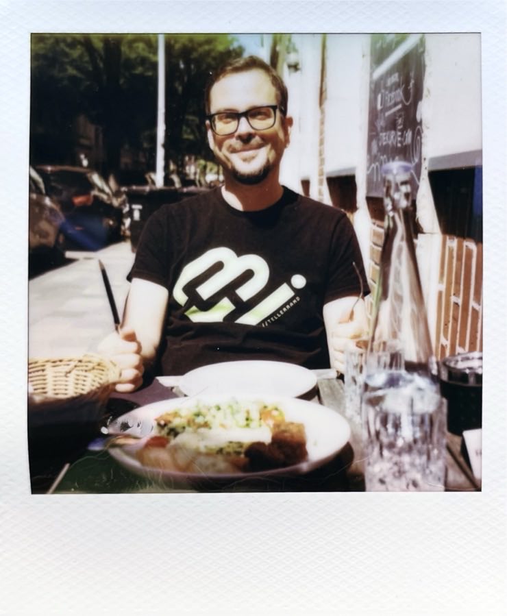 A man sitting on the other side of a sidewalk table with food on it.