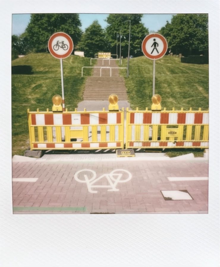 Barriers in yellow, red and white, fencing off a path an stairs between some grass.