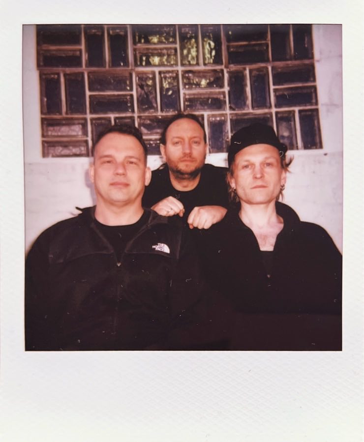 It’s the three men of Forkalyst again, photographed in front of a white wall with a thick window.