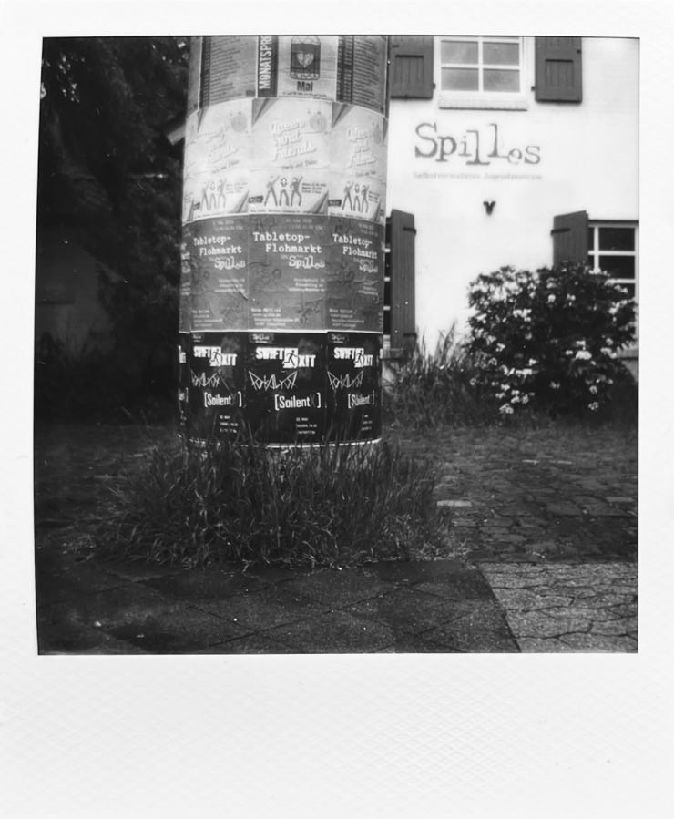 A ad column with poster for live gigs and a house in the background.