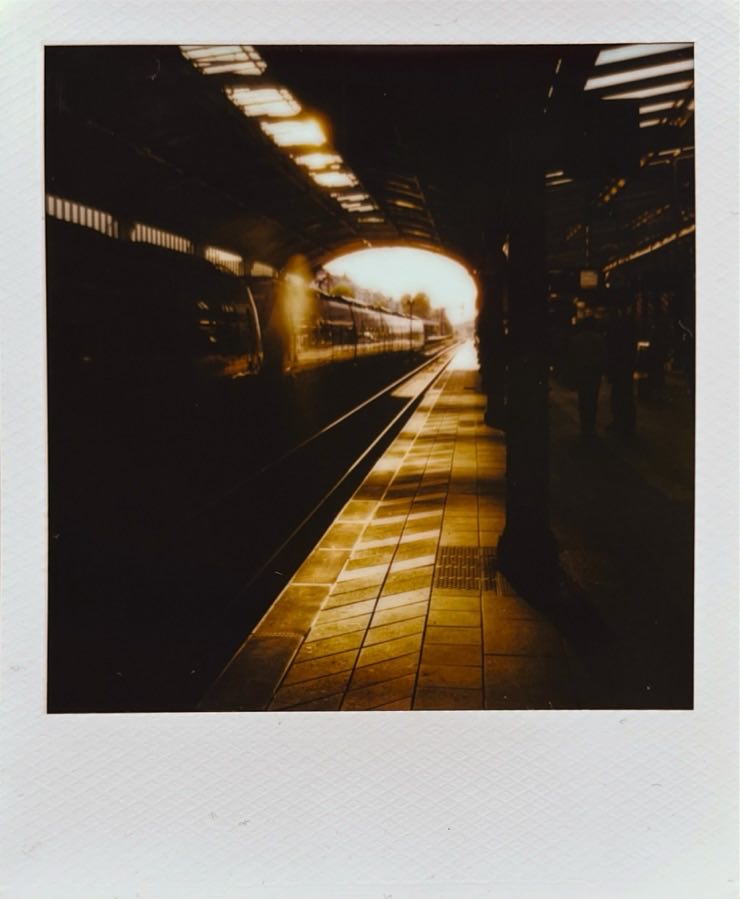 The low sun shining into a train station, with a train on the left, and the entrance/exit in the middle of the frame.