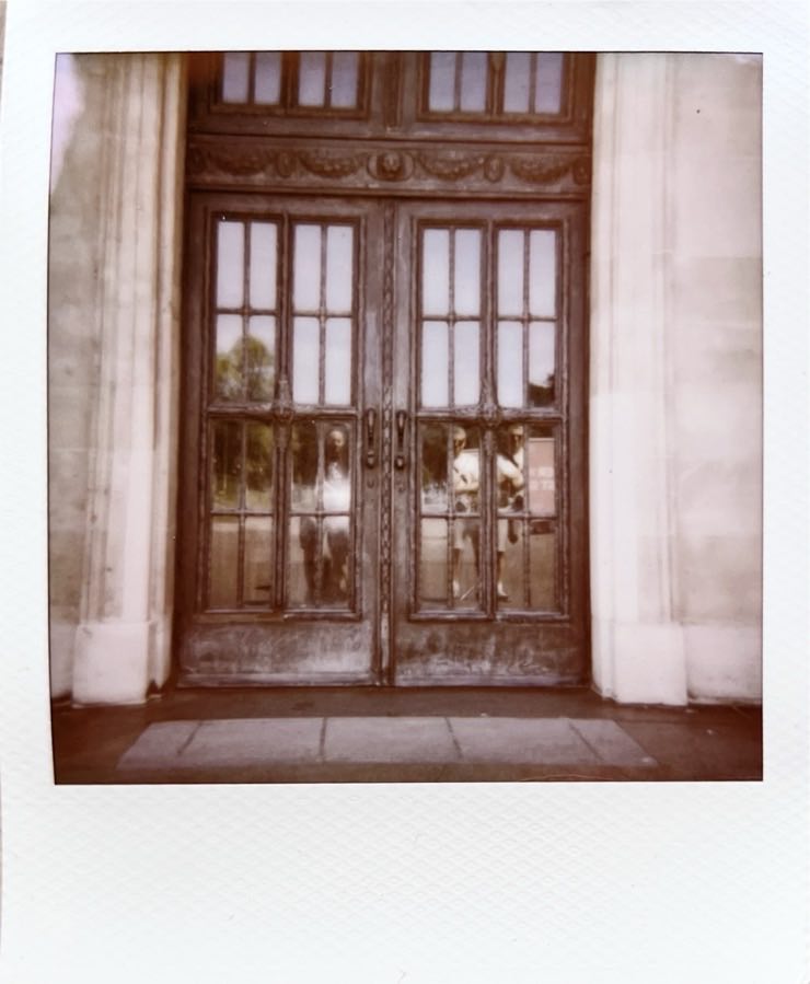 An old large door, showing a reflection of two men.
