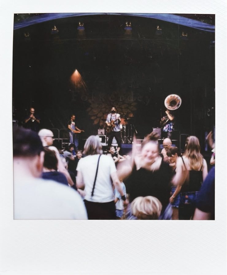 A stage with a band and a dancing crowd in front of it.