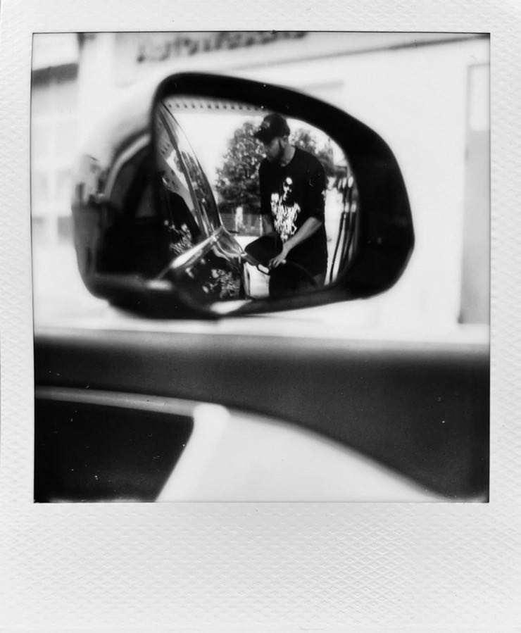 A person fuelling up a car, seen in a rear view mirror.