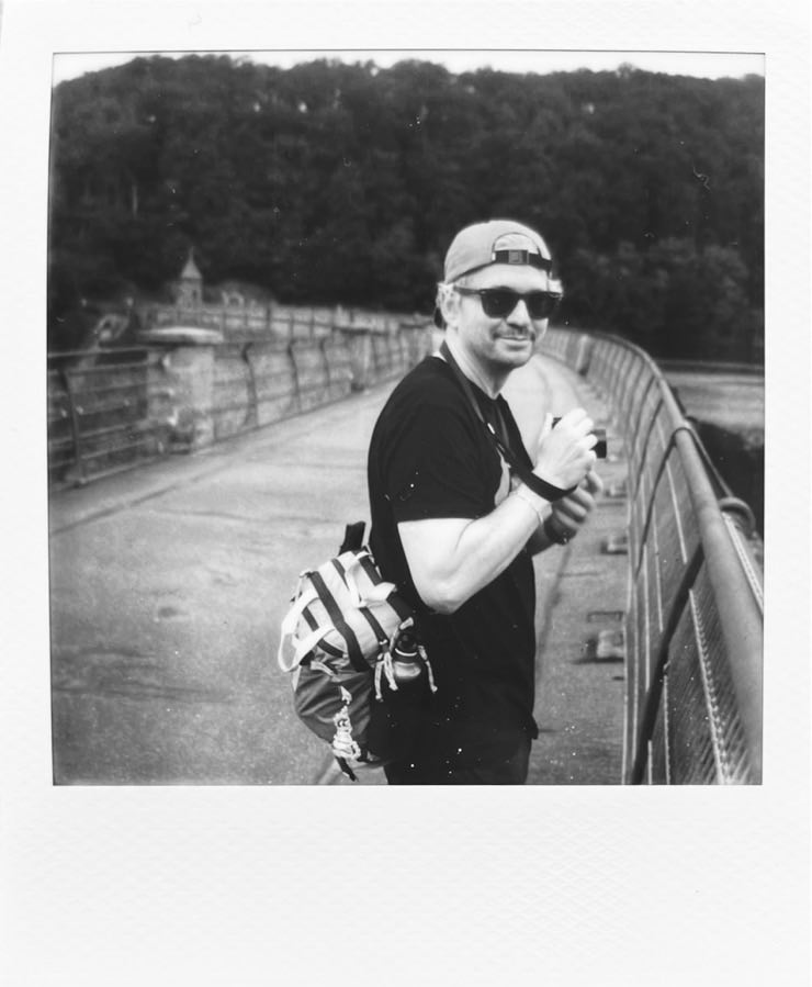 A man with camera on a dam, looking towards the viewer.