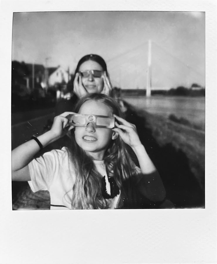 A child and a woman with eclipse-sunglasses on, illuminated by the sun.