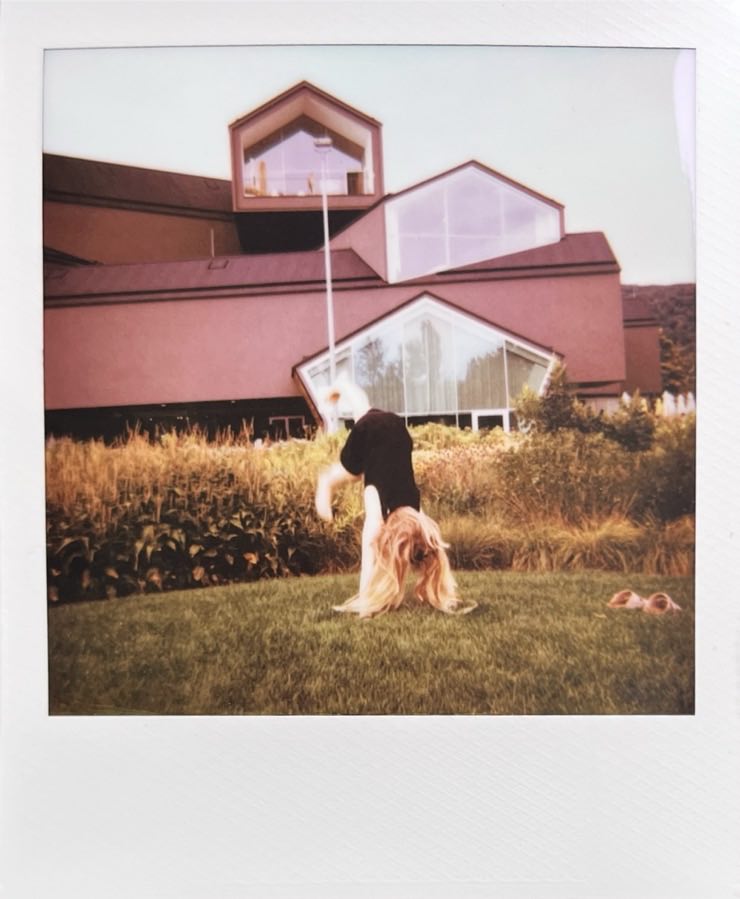 A girl trying a handstand in front of a wacky building.