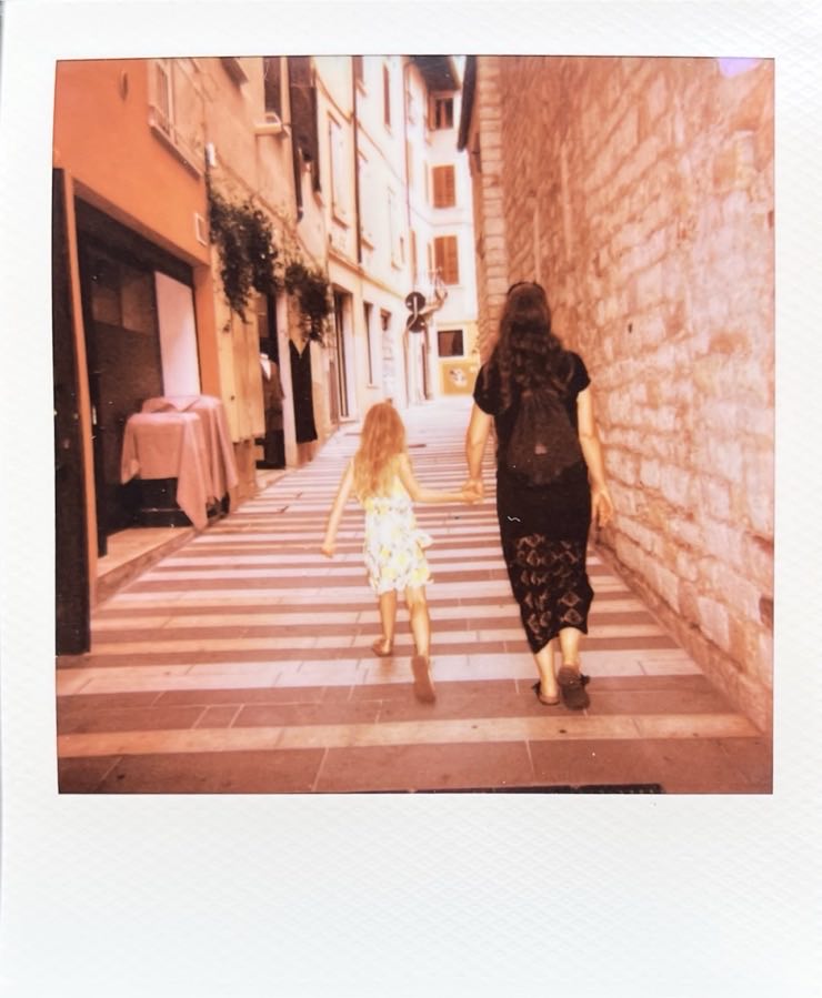 A girl and a woman walking hand in hand through a narrow Italian street.