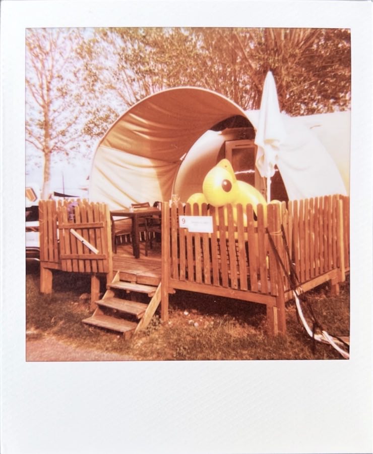 A large tent with a wooden terrace. The large inflatable duck hangs over the railing.