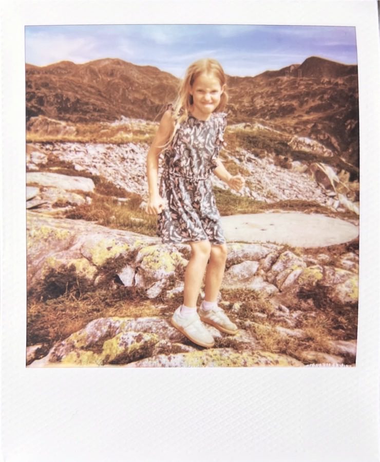 A girl in a green dress looking into the camera on the mountain.