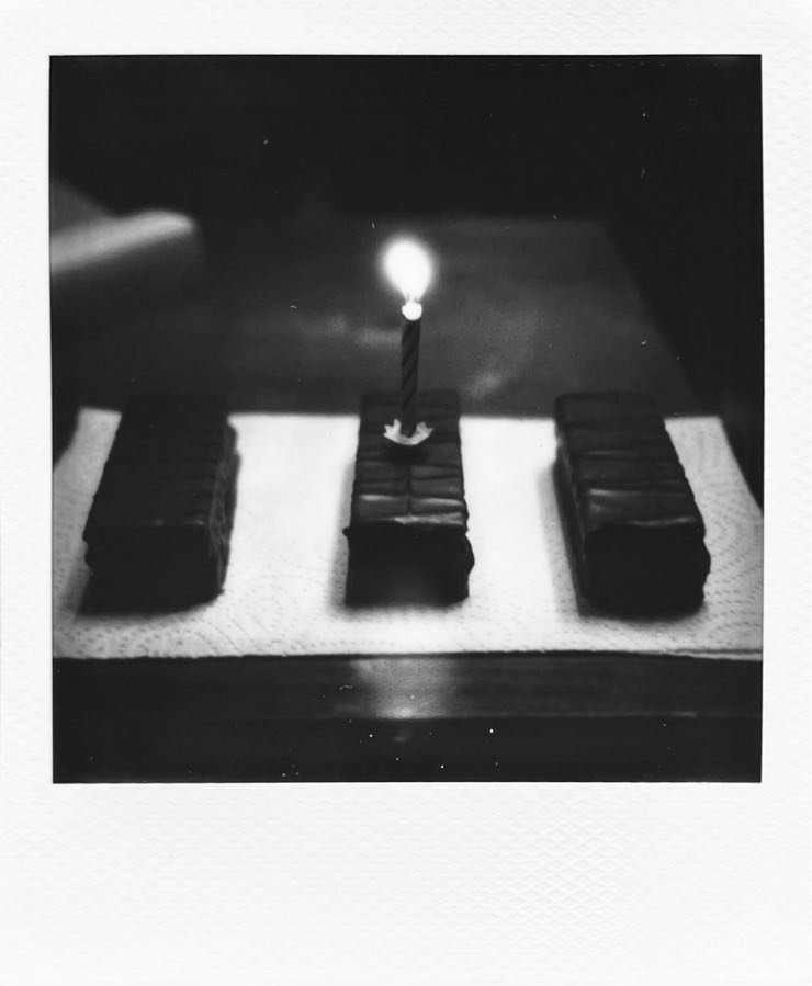 A rather dark b/w photo of three YES cake. The middle one with a little candle on top.