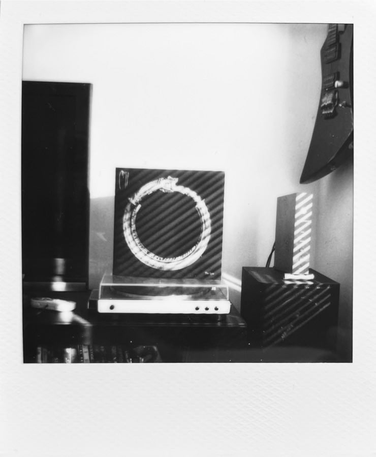 A record player with Messa‘s The Spin on top. A Tv on its left and a guitar hanging on the wall on its right.