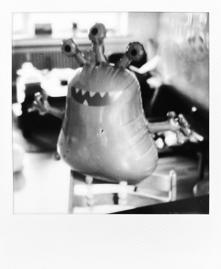 A balloon in the shape of a 3-eyed monster, standing on a chair next to a table.