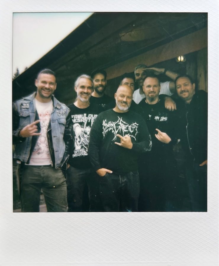 A group of men posing in front of a wooden hut.