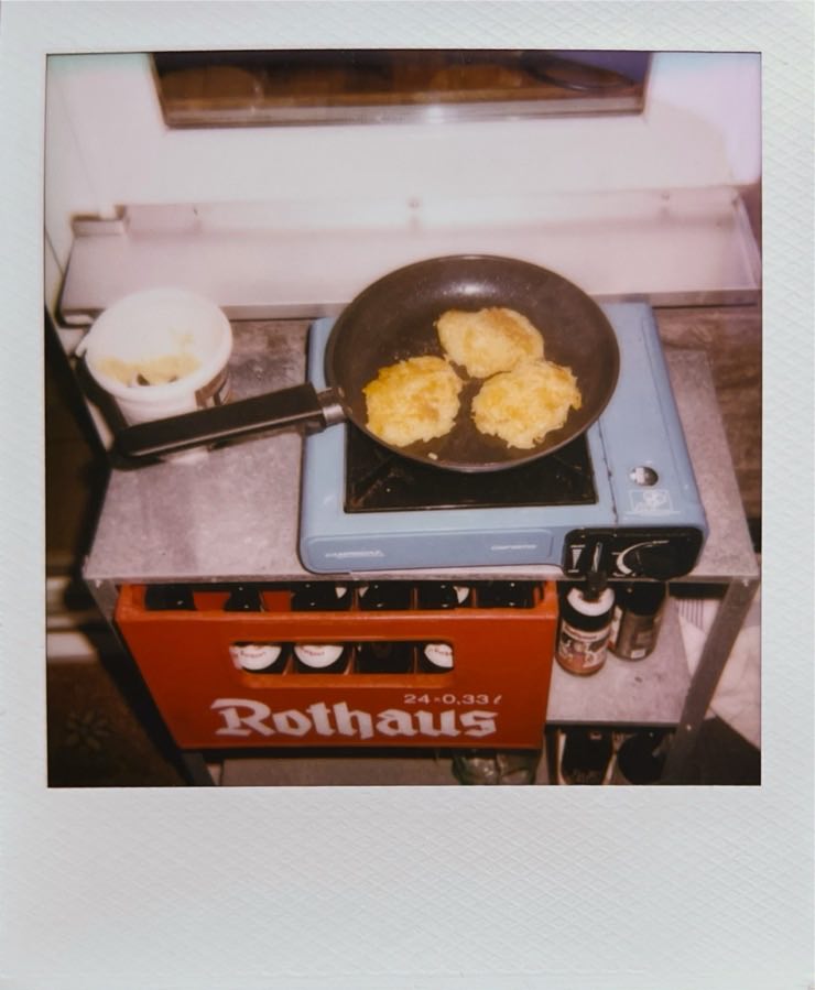 A pan on a blue gas cooker with Reibekuchen in it.